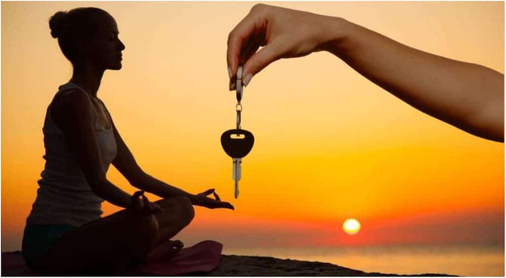 A woman is meditating at sunset and car keys are being handed to her.