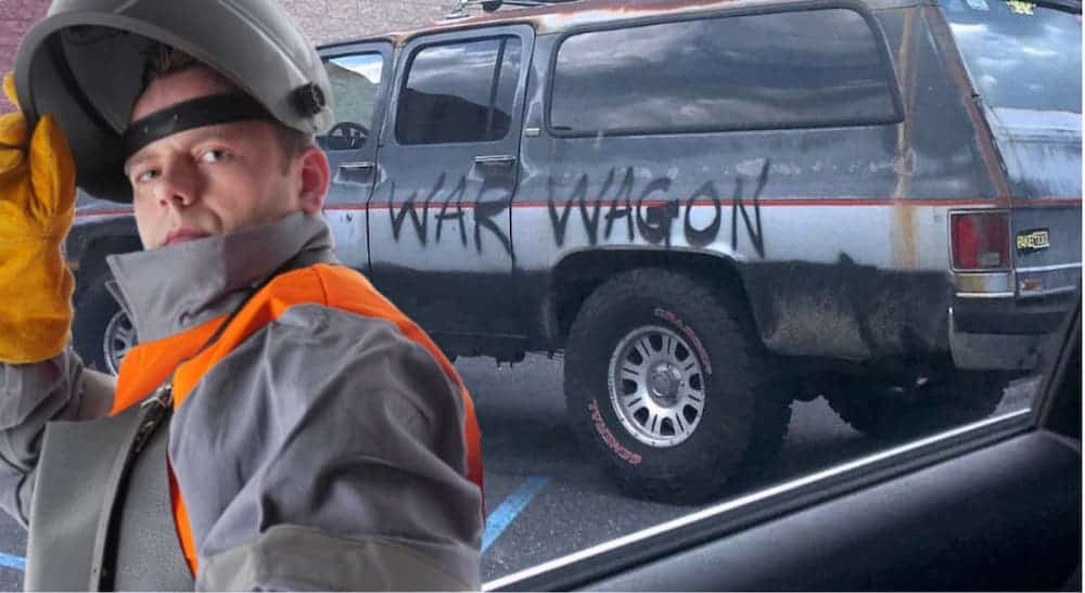 A man in welding gear is in front of an old Chevy SUV with "war wagon" painted on the side.