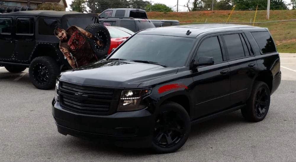 A zombie is rolling off of a black Chevy SUV and leaving blood streaks.