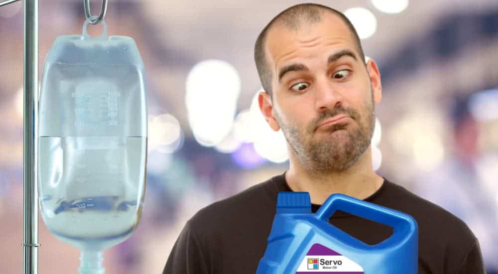 A man is staring cross eyed at a jug of oil next to an intravenous fluid bag.