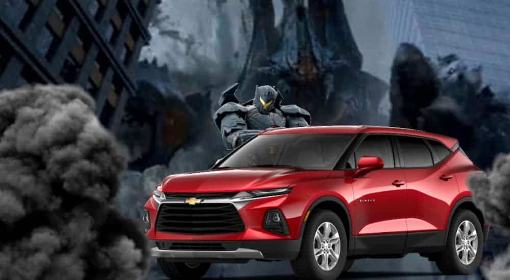 A red 2021 Chevy Blazer is in a city war zone in front of a Pacific Rim robot and monster.