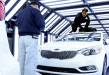Tom Cruise is on top of a white 2021 Kia Stinger in a factory production line.