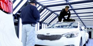 Tom Cruise is on top of a white 2021 Kia Stinger in a factory production line.