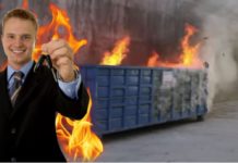A man in a suit is holding car keys while standing in front of a dumpster that is on fire.