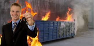 A man in a suit is holding car keys while standing in front of a dumpster that is on fire.