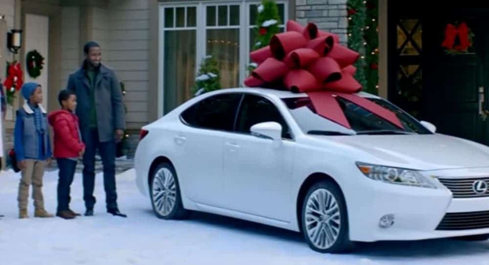 A family is next to a white car with a giant bow on top.