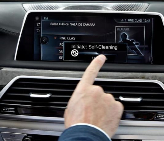 A hand is using a car's screen to select self-cleaning mode.