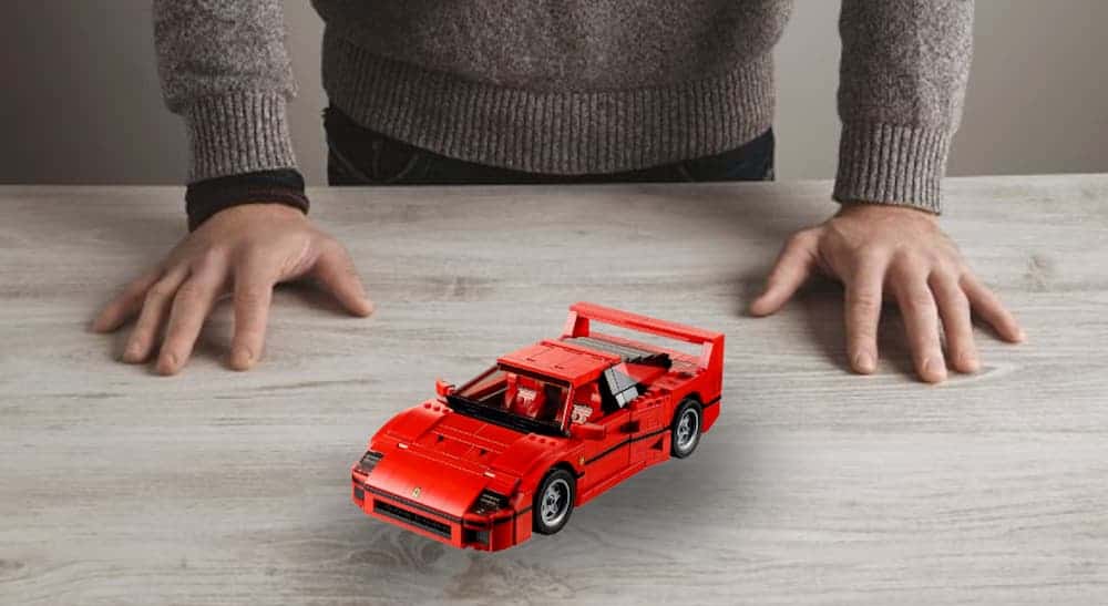 A toy red Ferrari is on a table in front of a man's hands.