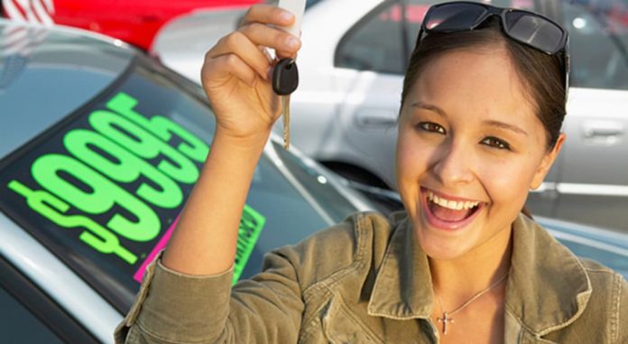 A woman is holding keys in front of a used car at a used Chevy dealer.