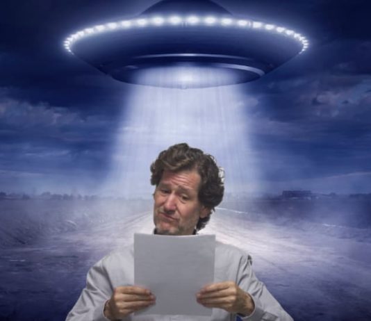 A man is reading a paper while a spaceship is beaming light over him.