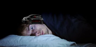 A close up shows a wide-eyed man laying on a pillow and a black used Fiat 500 perched on his head.