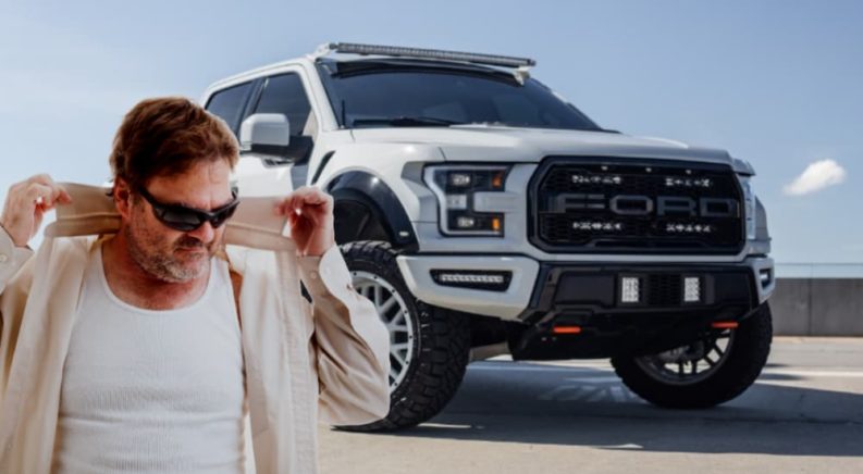 A middle aged man with sun glasses is shown popping his collar in front of a white 2021 Ford F-150 Raptor.