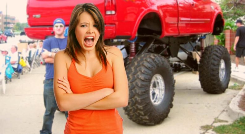 A disgusted woman has her arms crossed in front of a man and his lifted red truck.