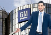 A man in a suit and tie is standing in front of the GM building holding his hands out.
