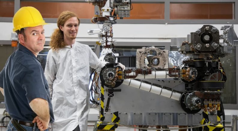 A mechanic and scientist are shown standing next to the Mars rover.