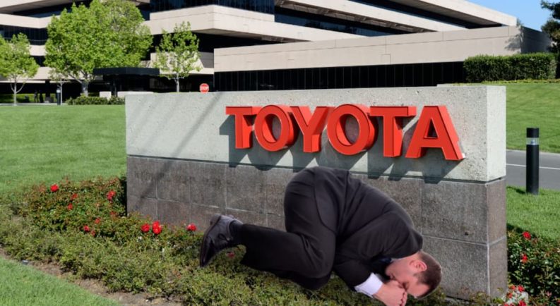 A man in a suit is laying in front of a Toyota sign and building.