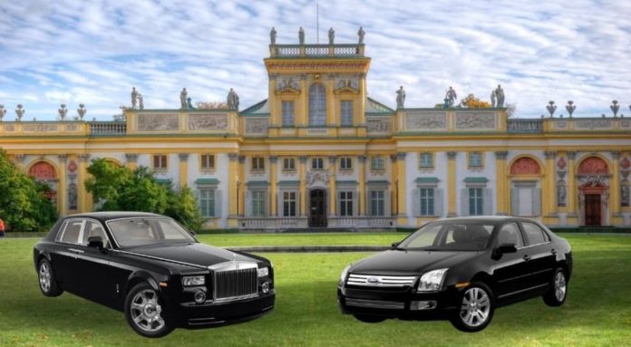 Two black used luxury vehicles are parked in front of a castle after leaving a used luxury car dealership.