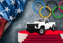 A white 2021 Chevy Silverado 1500 HD is shown on a stage next to an American flag and Olympic rings after leaving a Chevy Silverado HD dealer.