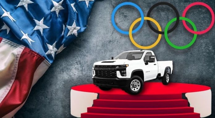 A white 2021 Chevy Silverado 1500 HD is shown on a stage next to an American flag and Olympic rings after leaving a Chevy Silverado HD dealer.