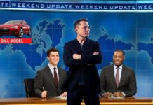 Elon Musk is standing in front of the desk on SNL weekend update.