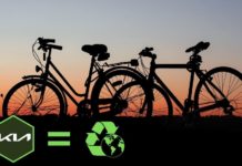 Bicycles are shown during a sunset near a Kia dealers logo and recycle symbol.
