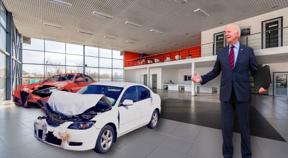 Joe Biden is shown in the showroom of a dealership with two smashed up cars.