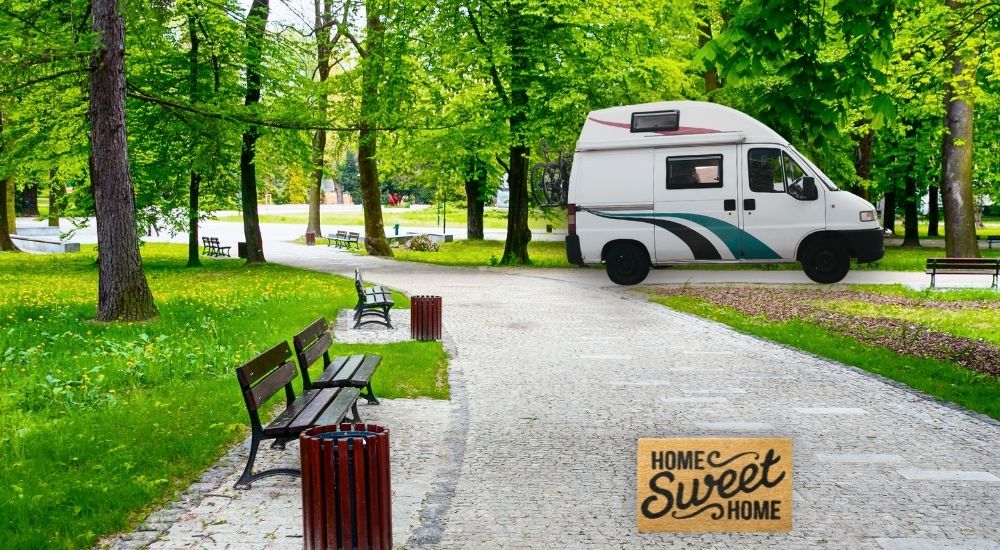 A camper van is shown parked in a park with a doormat on the ground in front of it.