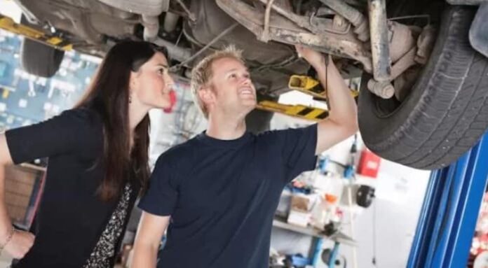 A woman and a man are shown looking at the bottom of a car at a Certified Pre-Owned Chevy truck dealer.