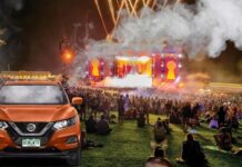 An orange Nissan Rogue for sale is shown at a festival.
