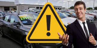 A car salesman is shown on a dealer lot next to a warning sign.