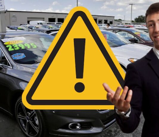 A car salesman is shown on a dealer lot next to a warning sign.