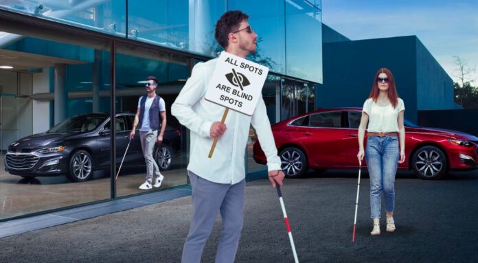 A group of blind protestors are shown near a red and a grey 2024 Chevy Malibu.