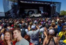 A white 2024 Chevy Equinox is shown on stage in front of a crowd and two people taking a photograph.