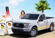 A white 2025 Ford F-151 is shown parked on a beach featuring an advertisement for Malibu Rum.